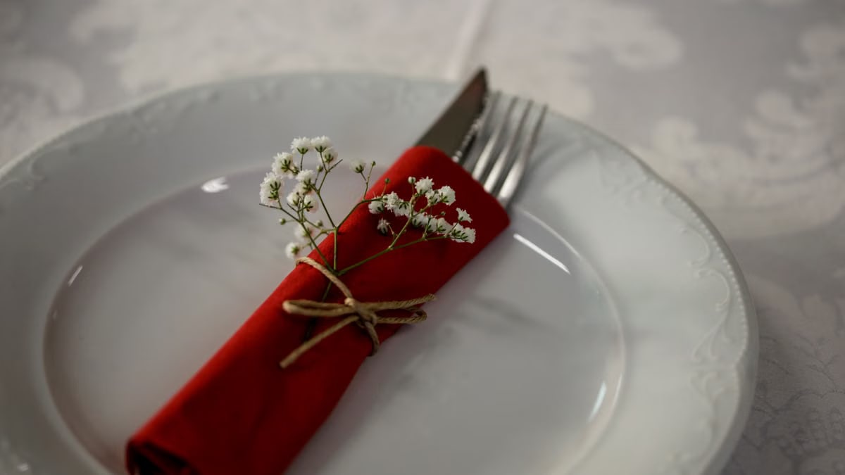 Elegant table setting with a red napkin, cutlery, and white flowers for a classy dining experience.