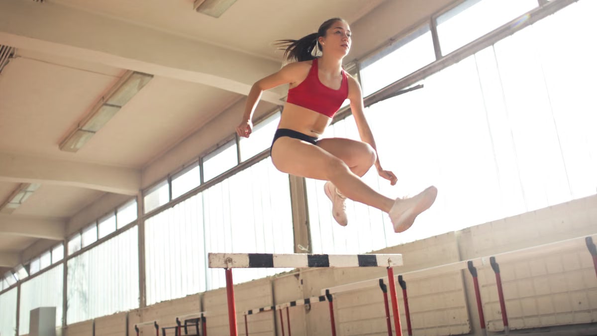 A female athlete demonstrates agility and grace by jumping a hurdle indoors.